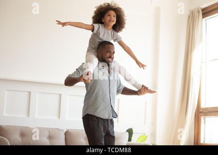 Liebende schwarze Vater, die kleine Tochter piggyback Ride zu Hause Stockfoto