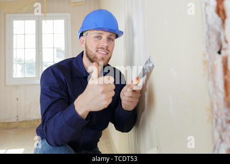 lächelnde junge Baumeister in Bauarbeiterhelm Daumen auftauchen Stockfoto