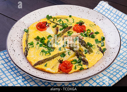 Omelett mit Spargel und Tomaten zum Frühstück auf einer hölzernen Hintergrund. Stockfoto