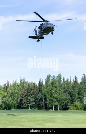 Eine Alaska Army National Guard UH-60 Black Hawk der 1 Bataillon, 207 Aviation Regiment schwebt über einem Feld zu Drop off zwei Alaska Air National Guard pararescuemen der 212th Rescue Squadron und eine Fackel für Nationale in diesem Jahr Veteranen Golden Age Spiele am Moose Run Golf Course, Joint Base Elmendorf-Richardson, 5. Juni 2019. Die nationalen Veteranen Golden Age Spiele ist eine Rehabilitation Programm in den Vereinigten Staaten entworfen, um die Lebensqualität für ältere Veteranen durch Förderung der Einbeziehung der körperliche und sportliche Aktivitäten zu verbessern. (U.S. Army National Guard Foto von Pvt. Gnade Necha Stockfoto