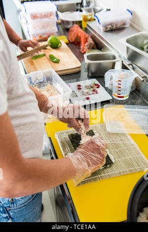 Hand des Chefs der japanischen Sushi rollen. Japanische Koch bei der Arbeit bereitet leckeres Sushi Roll mit Thunfisch und Avocado. Köstliche japanische Küche. Wählen Sie Stockfoto
