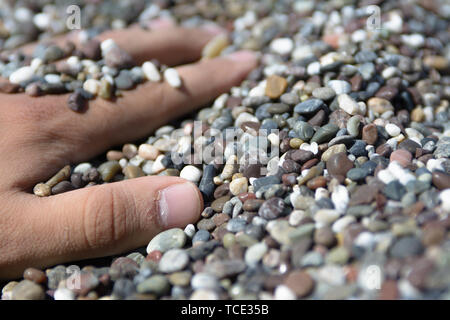 Eine männliche Hand unter den kleinen polierten Felsen am Strand begraben. Stockfoto