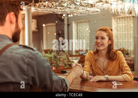 Martini Cocktail Liebhaber. Lächelnd charmante ansprechende entzückende Rothaarige verführerischen weiblichen tragen braune Bluse, ein Martini Cocktail aus einem bartend Stockfoto