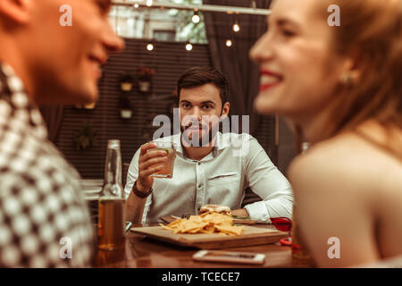 Starrte auf Freunde. Attraktive schöne ansprechende ruhige stattlicher Mann mit kurzen dunklen Haaren und Bart mit einem Drink in der Hand und starrte auf seine Fl Stockfoto