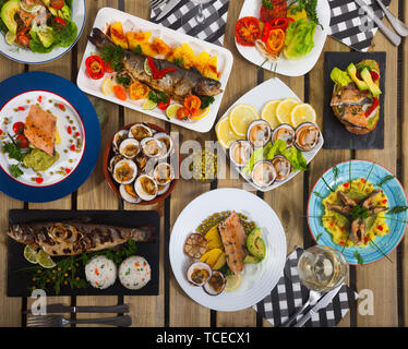 Blick von oben auf die Hauptgerichte und Snacks von Forellen und Herzmuscheln auf hölzernen Tisch Set Stockfoto