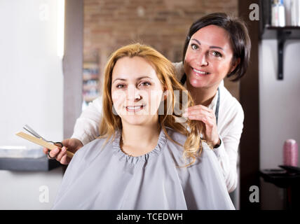 Gerne blonde Frau ist mit Arbeit von Meister und ihre Frisur in hairdress Salon zufrieden Stockfoto