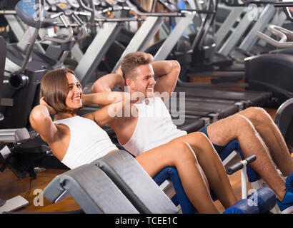 Junge russische Mann und Frau, die Sit Ups zusammen mit Maschine in der Turnhalle Stockfoto