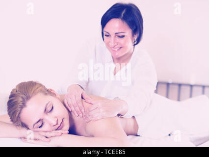 Reifen Masseurin tut, entspannende Massage Schulterbereich für junge Frau in Spa Salon. Stockfoto