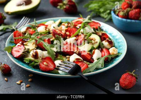 Gesunder Salat mit Erdbeeren, Avocado, Rucola und Mozzarella, mit Olivenöl und Balsamico Dressing in einer Platte auf einem dunklen Hintergrund entfernt gekleidet Stockfoto