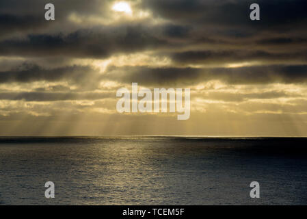 Strahlen der hellen Sonne durch dicke dunkle Wolken über der Oberfläche der Wellen Meer Stockfoto