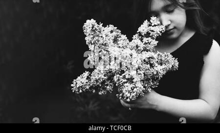 Süße kleine Mädchen duftenden Flieder. Person mit Blumen. Schwarz-weiß Foto. Kind mit Blumenstrauß vor der Tür. Zu Park, Wald im Sommer und sp Stockfoto