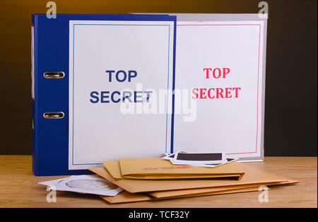 Umschläge und Ordner mit top secret Stempel und Foto Papiere mit CD-Laufwerke auf Holztisch auf braunem Hintergrund Stockfoto