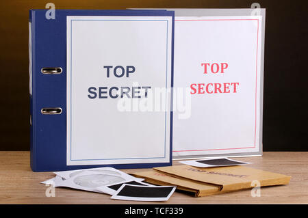 Umschläge und Ordner mit top secret Stempel und Foto Papiere mit CD-Laufwerke auf Holztisch auf braunem Hintergrund Stockfoto