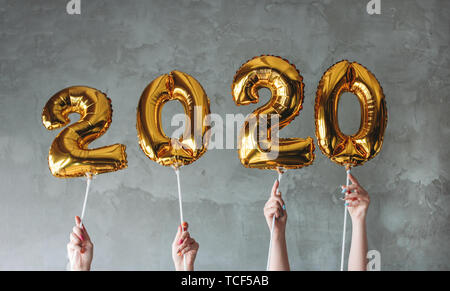 Die Frau, die Hände, die 2020 Nummern Ballons auf die graue Betonwand Hintergrund. Neues Jahr Party mit Freunden, Corporate Stockfoto