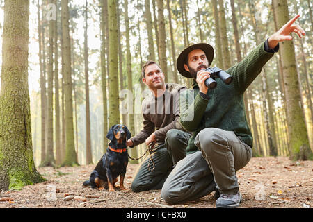 Zwei Jäger mit Fernglas und mit Hund als Hund auf dem Stiel im Wald Stockfoto