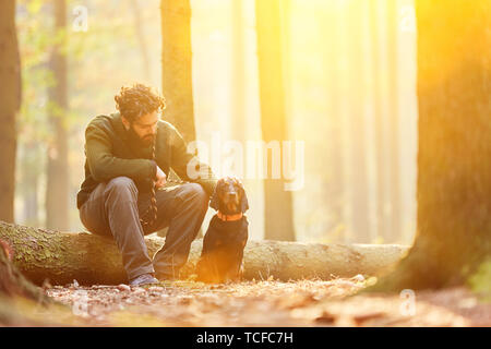 Förster sitzt im sonnigen Wald mit Hund als Jagdhund Stockfoto