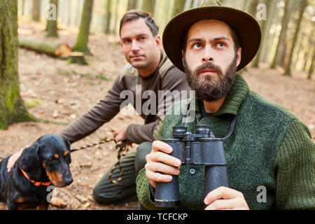 Zwei Jäger oder Förster mit Fernglas Jagd und Hund auf der Pirsch im Wald Stockfoto