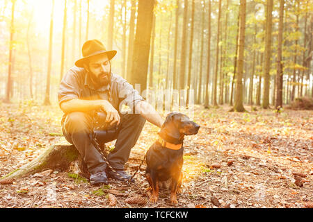 Ranger mit seinem Hund im Wald sitzt auf einem Baumstumpf während einer Pause Stockfoto