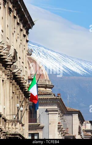 Vertikale Foto der historischen Gebäude im sizilianischen Catania, Italien mit Winkenden italienische Flagge auf der Fassade. Im Hintergrund die Kuppel der berühmten Hl. Agatha Kathedrale und Vulkan Ätna. Italienische Konzept. Stockfoto