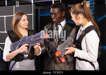 Afrikanischer Mann und zwei feinen kaukasischen Frauen holding Laser Gewehren und auf der Laser tag Zimmer posing Stockfoto