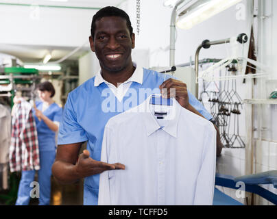 Fröhliche African American man Arbeiter der Dry Cleaner, saubere Kleidung nach chemische Reinigung Stockfoto