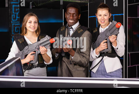 Afrikanische Mann und zwei glückliche kaukasischen Frauen holding Laser Gewehren und auf der Laser tag Zimmer posing Stockfoto