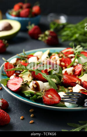 Gesunder Salat mit Erdbeeren, Avocado, Rucola und Mozzarella, mit Olivenöl und Balsamico Dressing in einer Platte auf einem dunklen Hintergrund entfernt gekleidet Stockfoto