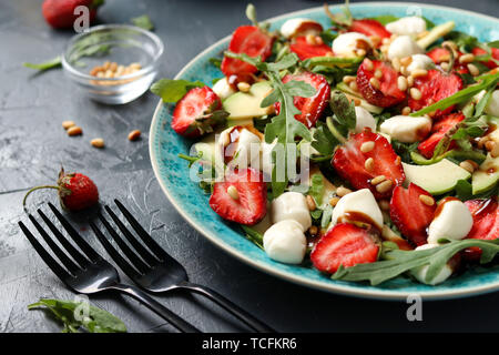 Gesunder Salat mit Erdbeeren, Avocado, Rucola und Mozzarella, mit Olivenöl und Balsamico Dressing in einer Platte auf einem dunklen Hintergrund entfernt gekleidet Stockfoto