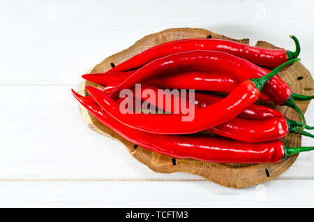Viele rote Chili pepers liegt auf einem oval braun Vorstand, der auf einem weißen Holz Tisch steht Stockfoto