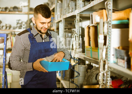 Junge lächelnde positiver Mann Arbeiter gehen durch Sanitärtechnik Details in der Werkstatt Stockfoto