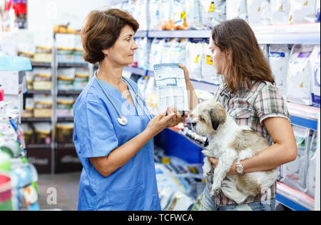 Ältere Menschen froh, dass weibliche Tierarzt empfehlen Heimtierfutter junge Frau besucht Pet Store mit Ihrem Welpen Stockfoto