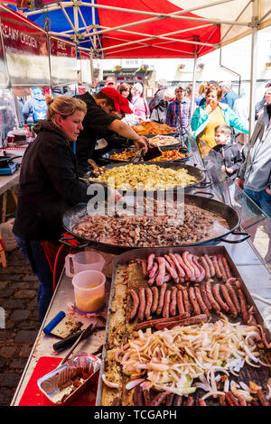 Die Le Wochenende Veranstaltung in der mittelalterlichen Stadt Sandwich, England. Französischen Markt veranstaltet jährlich in den Stadtplatz. Blick entlang der langen, heißen Garküche verkauf Paella, Französisch Würstchen und diverse andere Lebensmittel in großen Pfannen auf der Theke zubereitet. Frau rühren Schüssel mit Essen kochen in grossen Pfanne. Stockfoto