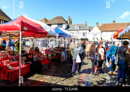 Le Wochenende Fall französischen Markt in Sandwich, England. Marktstände in gepflasterten Stadtplatz in hellem Sonnenlicht, Menschen zu Fuß kaufen und suchen, mittelalterliche Häuser im Hintergrund. Stockfoto