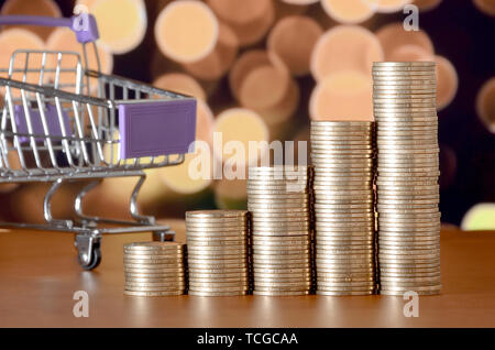 Leer Warenkorb und Geld Stapeln in Wachstum graph auf dem Hintergrund der farbigen Bokeh christmas lights. Shopping Zeitraum Konzept Stockfoto