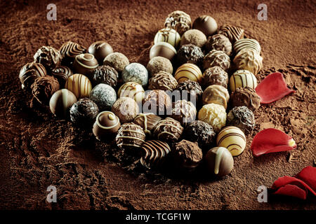 Red rose petals Neben verschiedene kleine leckere Runde Schokolade Bonbons in der Form von Herzen Stockfoto