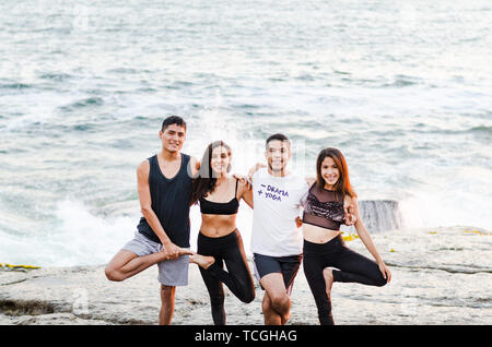 Gruppe von Menschen, die Yoga Übungen und lächelnd auf den Strand Stockfoto