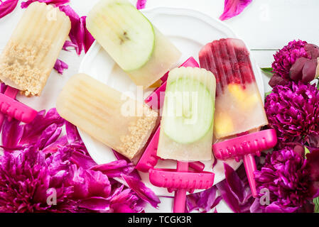 Hausgemachte veganes Eis am Stiel aus gefrorenen Apfelsaft und Beeren, Äpfel und Cookies auf hellen Hintergrund. Pfingstrosen und Blütenblätter in der Nähe, Sommer essen Konzept. Stockfoto
