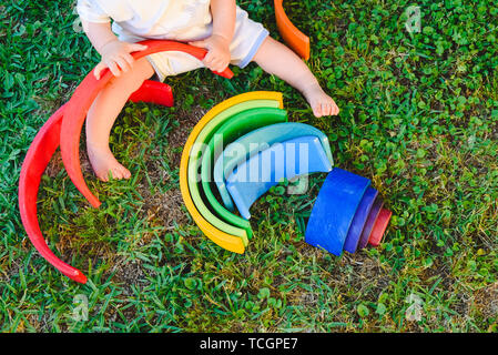 Baby girl spielt mit einer Waldorf Material, ein Regenbogen aus Holz Montessori, in der Natur. Stockfoto