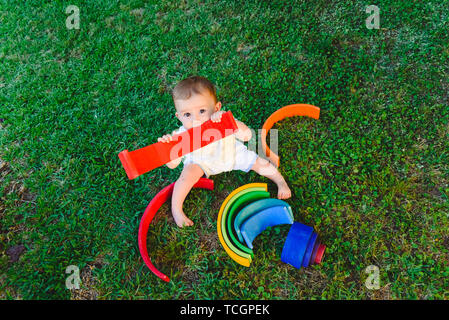 Baby spielt mit einem bunten Regenbogen aus Holz auf dem Gras, geistige und seelische Entwicklung. Stockfoto