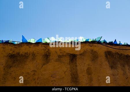 Bunte Glasscherben auf einer Adobe Wand als rohe Sicherheit gegen Einbrecher glow gegen einen klaren blauen Himmel im historischen Zentrum von San Miguel de Allende, Guanajuato, Mexiko. Stockfoto