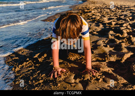 Kinder spielen in den Sand am Strand, kniend sein Gesicht versteckt.