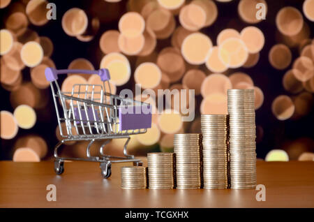 Leer Warenkorb und Geld Stapeln in Wachstum graph auf dem Hintergrund der farbigen Bokeh christmas lights. Shopping Zeitraum Konzept Stockfoto