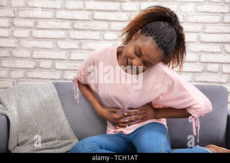 Junge Frau sitzt auf einem Sofa Bauchschmerzen Leiden zu Hause Stockfoto