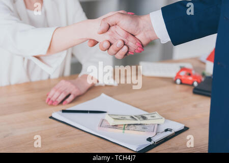 Teilweise mit Blick auf die Frau die Hände schütteln mit Geschäftsmann in der Nähe von Dollar Banknoten auf Tisch Stockfoto