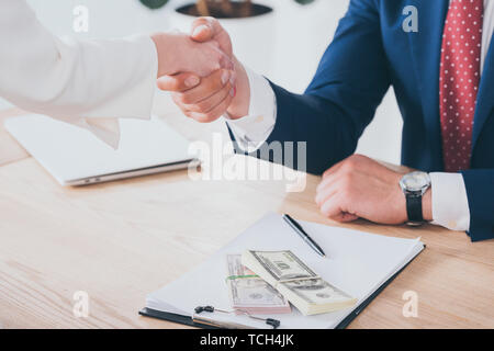 Teilweise mit Blick auf die Frau die Hände schütteln mit Geschäftsmann in der Nähe von Dollar Banknoten auf Tisch Stockfoto