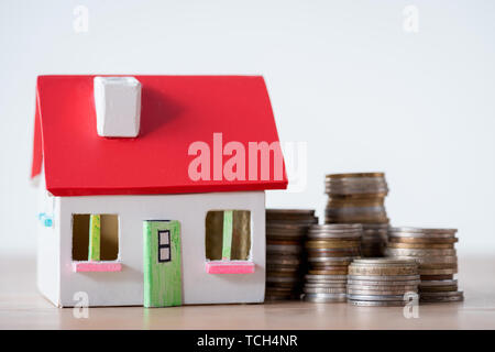 Haus Modell mit rotem Dach und weißen Wänden und Stapel von Münzen isoliert auf Grau Stockfoto