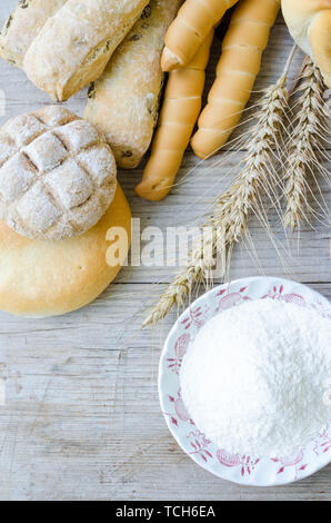 Verschiedene Arten von traditionellen Italienischen frisch gebackenes Brot und Brötchen mit Schüssel Mehl auf hölzernen Tisch Hintergrund. Rustikale Vintage Style. Ansicht von oben. Stockfoto