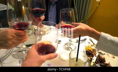 Vier Hände halten roten Wein und Beifall in einem Restaurant zu feiern. Stockfoto