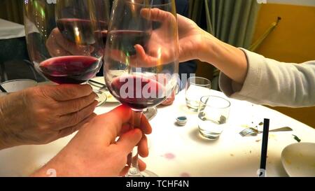 Nahaufnahme von vier Händen mit Rotwein Gläser dabei Cheers in einem Restaurant zu feiern, stellen Sie in der Tabelle auf der Hintergrund verschwommen. Stockfoto