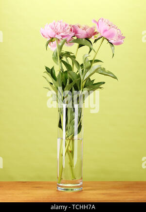 Drei rosa Pfingstrosen in Vase auf Holztisch auf grünem Hintergrund Stockfoto